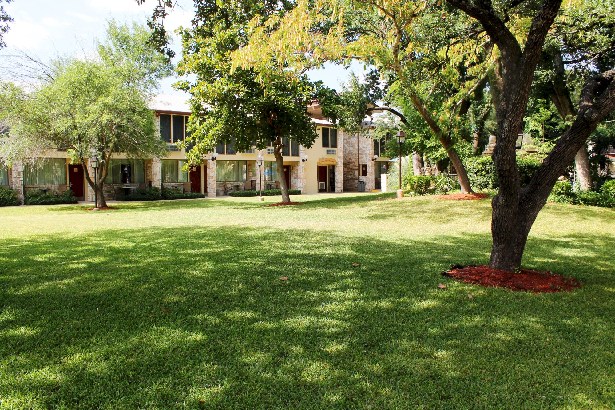 A large house with a lush green lawn and trees in the foreground.