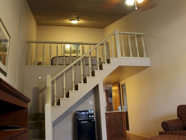 The image shows an interior loft with a staircase, a wooden ceiling, furniture, and a visible upstairs bed area.