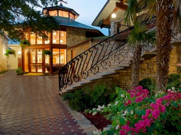 A beautifully lit house exterior with large windows, a staircase, and colorful flowers in the foreground enhance the scene.