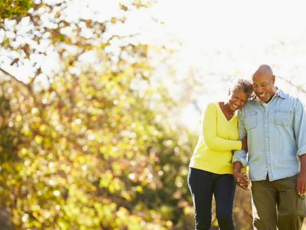 A couple is walking in a park, enjoying a sunny day and smiling at each other.