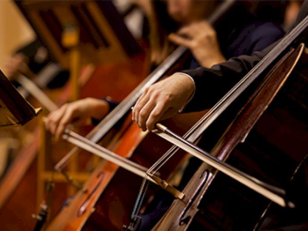 A person is playing a cello with a bow in an orchestra setting.