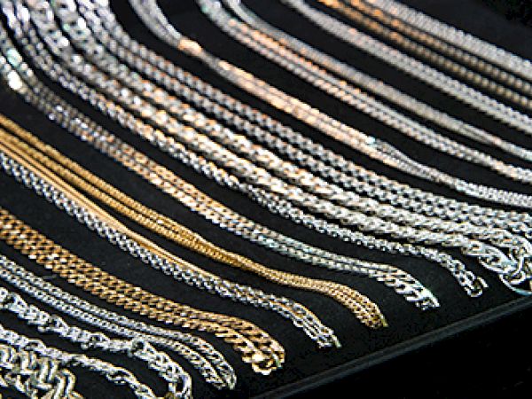 The image shows various gold and silver chains displayed on a black surface in neat rows.