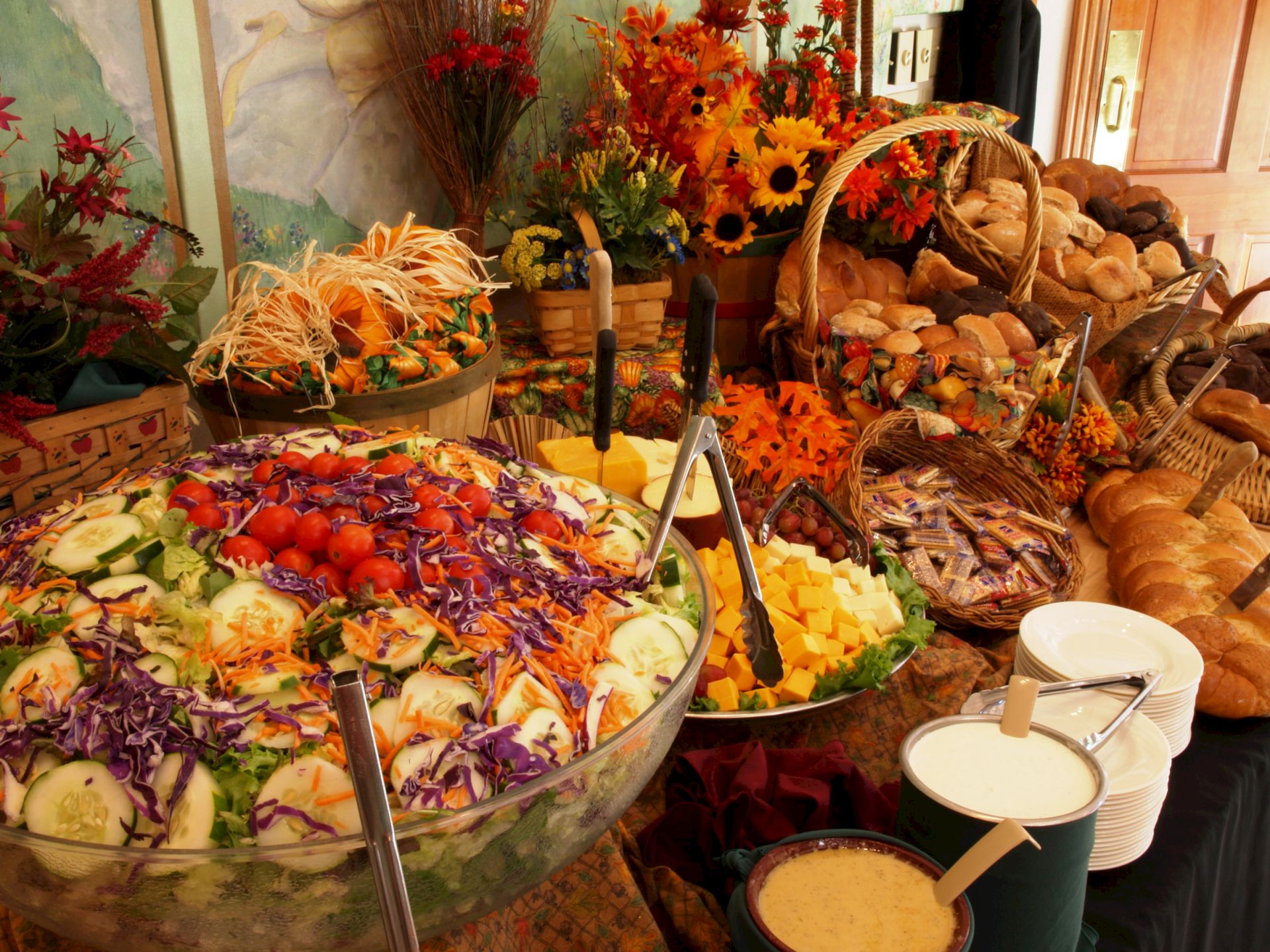 A buffet spread with salad fixings, bread, cheese, and colorful flowers in baskets around the food.