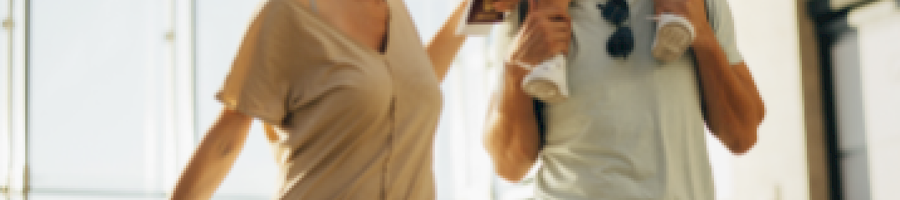 A family happily walks through an airport, with a woman pulling luggage and a man carrying a child on his shoulders.