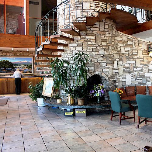 A hotel lobby with a spiral staircase, stone wall, plants, and seating area is visible in the image.