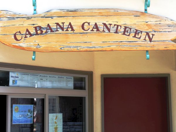 A wooden sign reads "Cabana Canteen" above a doorway with glass windows and notices visible inside.
