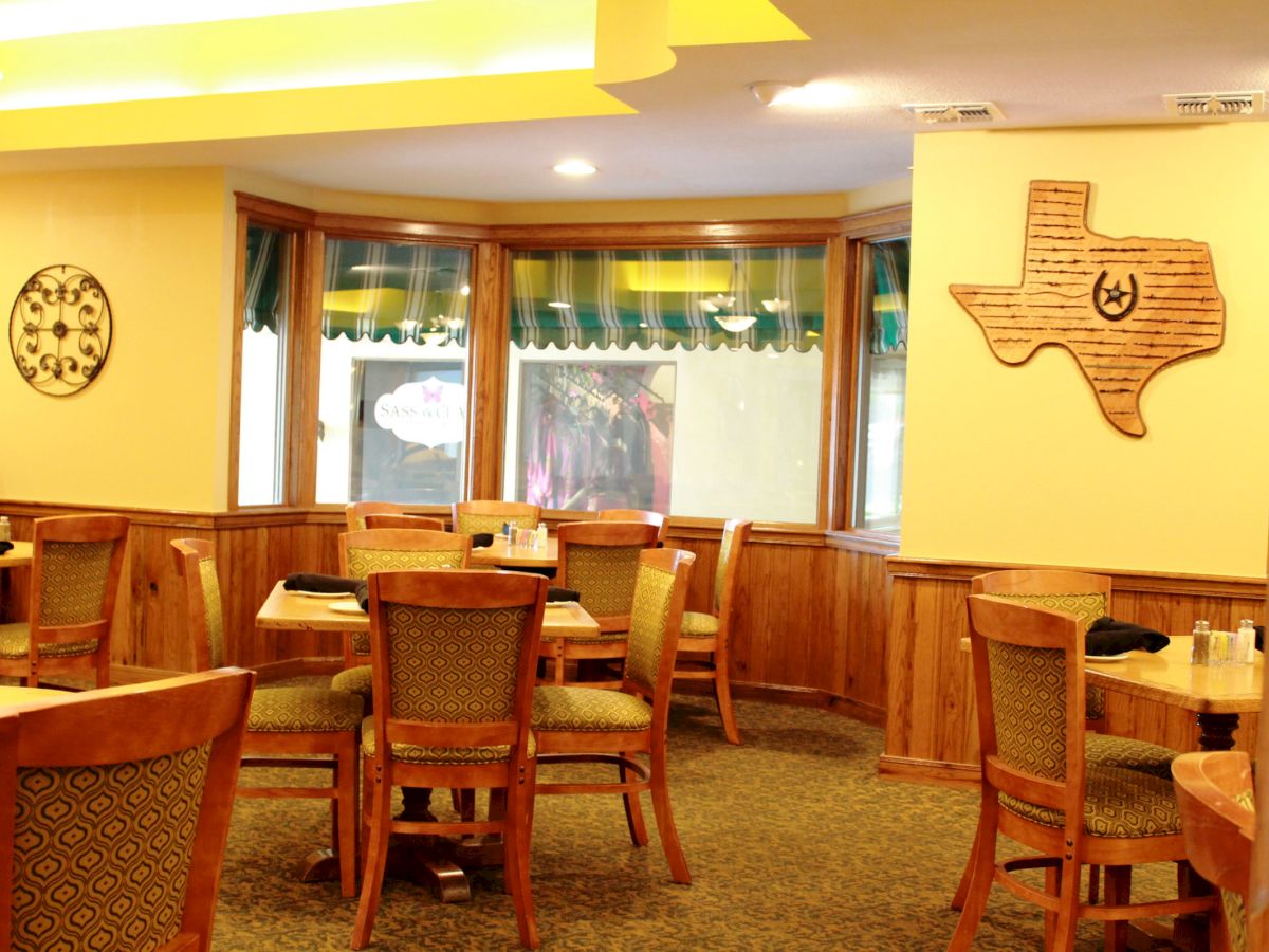 The image shows a cozy restaurant interior with wooden chairs and tables, wall decor, and a map of Texas on the wall.