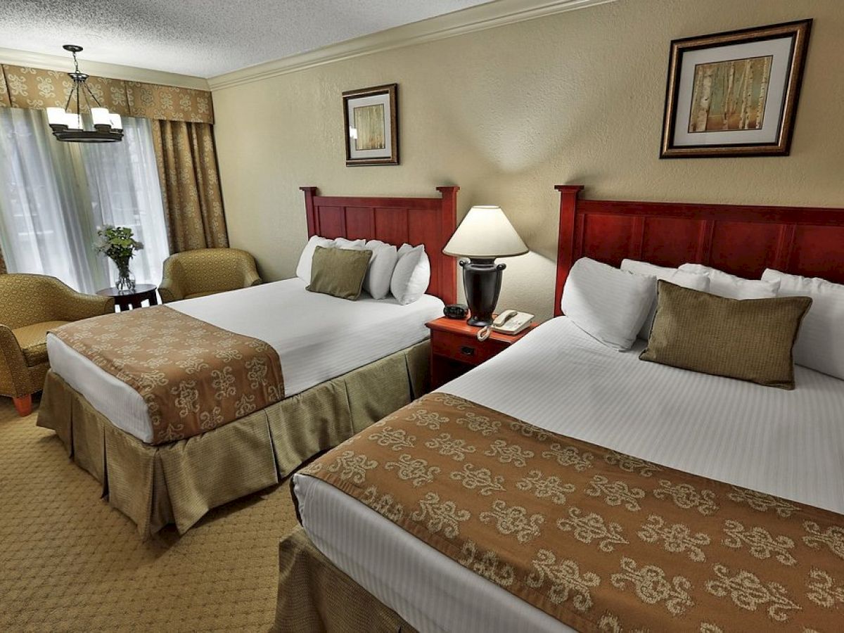 The image shows a hotel room with two double beds, cushions, lamps, and framed artwork; it has a warm color palette.