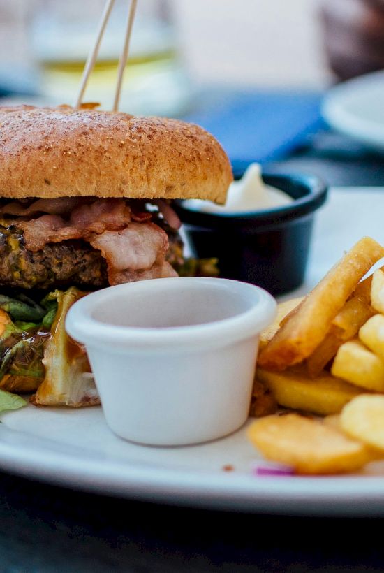 A burger with lettuce and sauce sits on a plate next to a side of fries, accompanied by small dipping sauce containers.