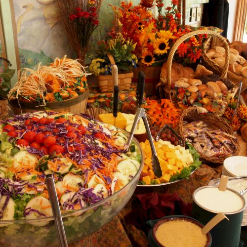 A vibrant buffet spread featuring a large salad bowl, bread, fruits, and decorative flowers, creating an appetizing and colorful display.