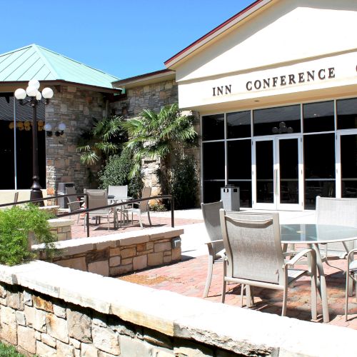 The image shows an outdoor patio area with tables and chairs outside a building labeled "Conference Center," featuring stone walls and plants.