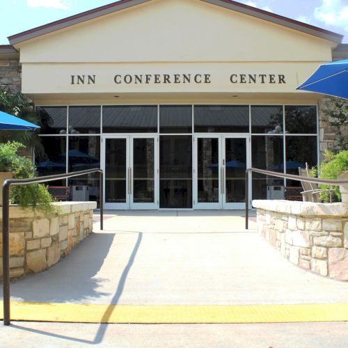 The image shows the entrance of an "Inn Conference Center" with glass doors, stone walls, and blue umbrellas in the surroundings.
