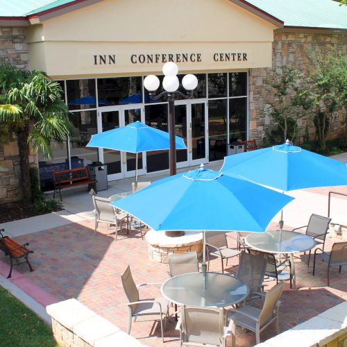 The image shows an outdoor seating area with blue umbrellas and chairs in front of a building labeled "Inn Conference Center."