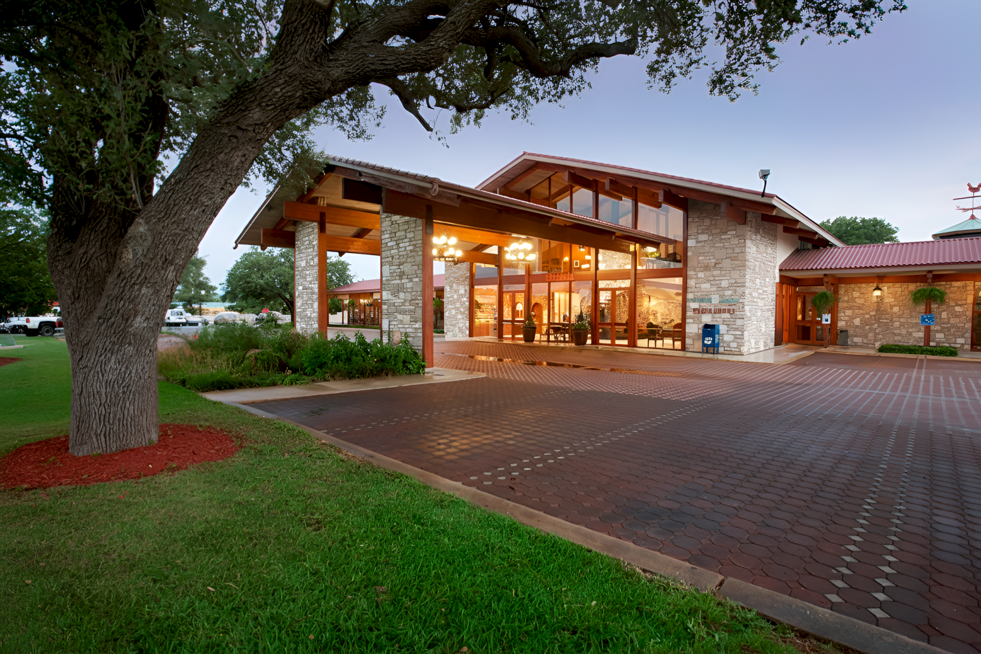 A modern building with large windows and a stone facade, surrounded by trees and a paved driveway in front.