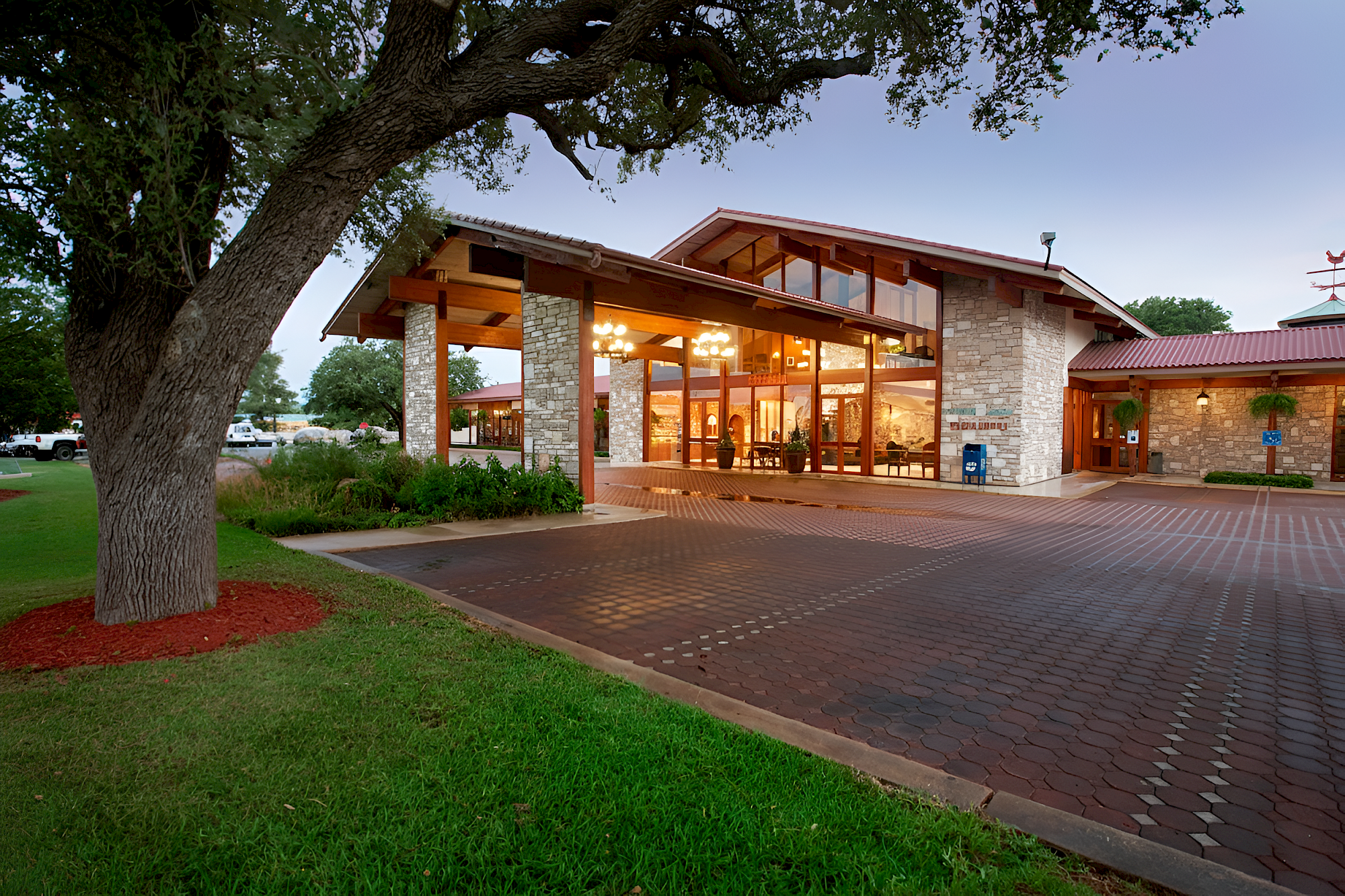 A modern building with large windows and a stone facade, surrounded by trees and a paved driveway in front.