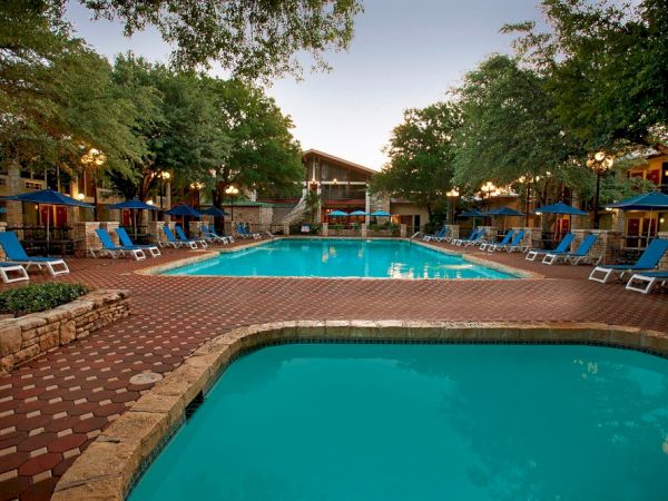 The image shows a pool area with lounge chairs, umbrellas, and surrounding trees, creating a relaxing outdoor setting.