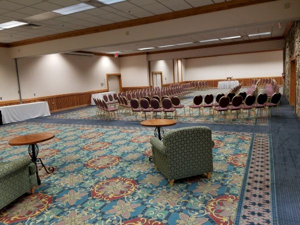 An empty conference room with chairs arranged in rows and floral carpet, featuring tables and couches along the walls.