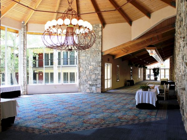 A spacious room with stone walls, a large chandelier, and tables covered with white cloths, possibly set for an event or gathering.