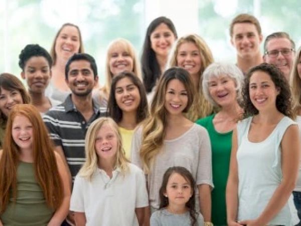 The image shows a diverse group of smiling people of various ages gathered together.