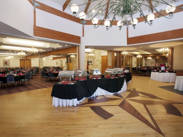 The image shows a spacious banquet hall with buffet tables, elegant chandeliers, and a star-like design on the wooden floor.