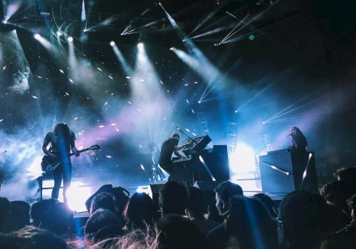 A live concert with a band performing on stage, bright spotlights, and an audience watching intently.