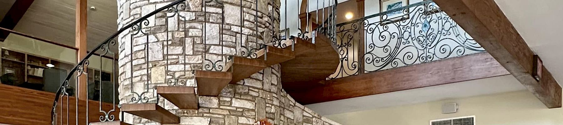 A stone spiral staircase winds around a tall, brick oven feature inside a rustic, vaulted room with wooden beams and tiled floor.