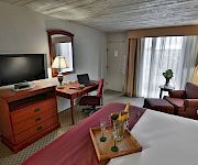 A hotel room office area with a desk, TV, laptop, lamps, curtains, sofa, and a small table with a champagne bucket.