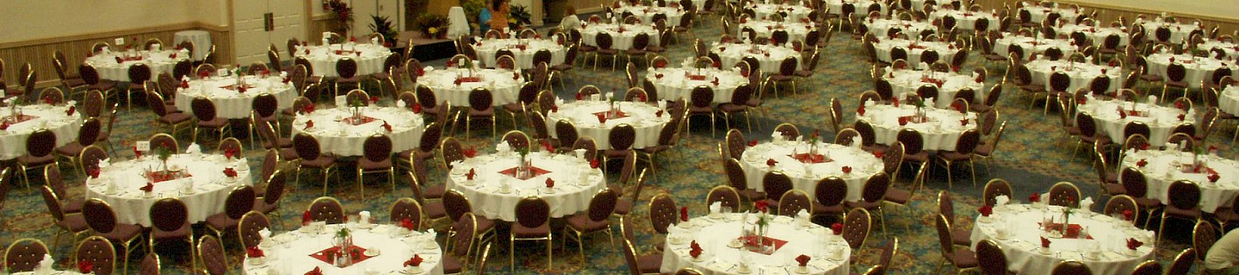 A decorated banquet hall filled with round tables, gold chairs, and place settings for a formal dinner event.