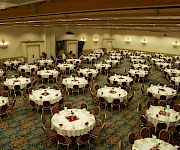 A decorated banquet hall filled with round tables, gold chairs, and place settings for a formal dinner event.
