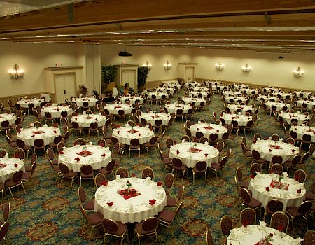 A decorated banquet hall filled with round tables, gold chairs, and place settings for a formal dinner event.
