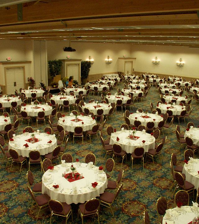 A decorated banquet hall filled with round tables, gold chairs, and place settings for a formal dinner event.