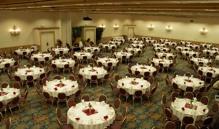 A decorated banquet hall filled with round tables, gold chairs, and place settings for a formal dinner event.