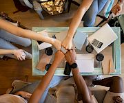 People sit around a table collaborating with laptops, notebooks, and coffee while planning or working together in a casual meeting.